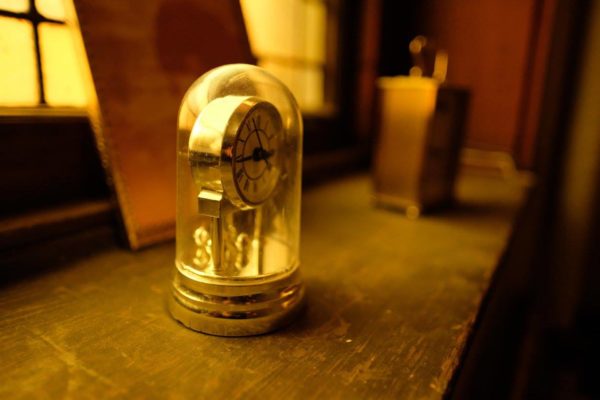 An old clock sitting on a table beside a window.