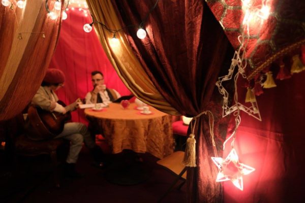 Two people sitting at a table inside a red room with string lights.
