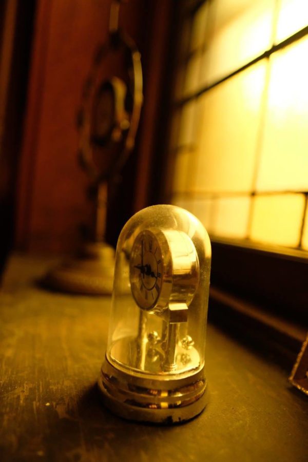 An old clock sitting on a table beside a window.