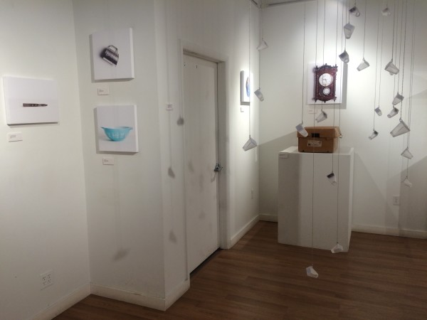 A wide view of the installation, showing glass bottles, empty furniture, and sentimental objects.