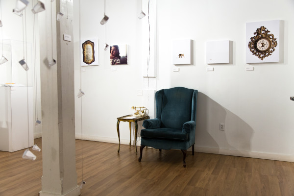 A wide view of the installation, showing glass bottles, empty furniture, and sentimental objects.