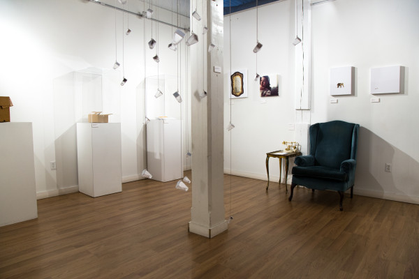 A wide view of the installation, showing glass bottles, empty furniture, and sentimental objects.