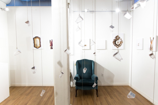 A wide view of the installation, showing glass bottles, empty furniture, and sentimental objects.